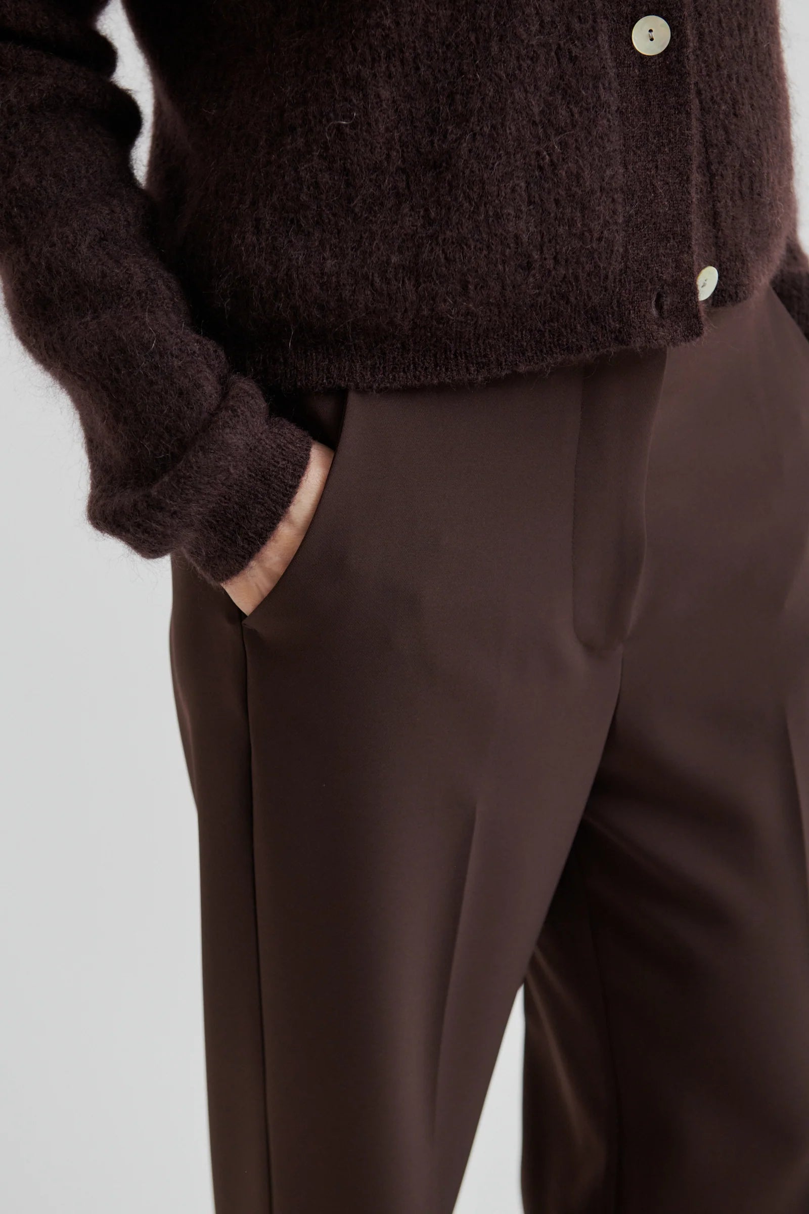 Person wearing a brown cardigan and pants on a light gray background