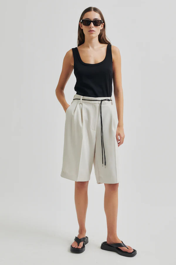 Model wearing black tank top and white pleated shorts with a black drawstring cord belt on a light grey background
