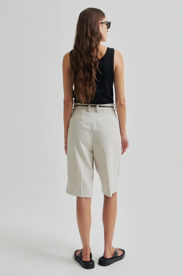 Model wearing black tank top and white pleated shorts with a black drawstring cord belt on a light grey background