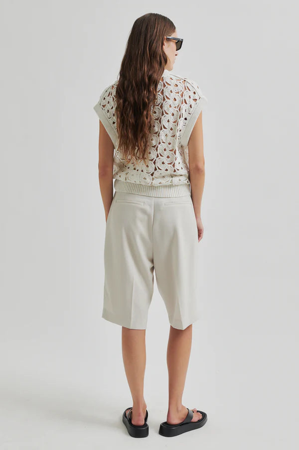 Model wearing white crochet top and white pleated shorts with a black drawstring cord belt on a light grey background