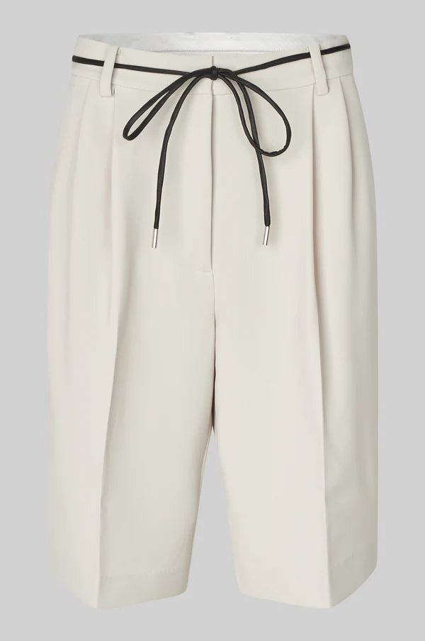 White pleated shorts with a black drawstring cord belt on a light grey background