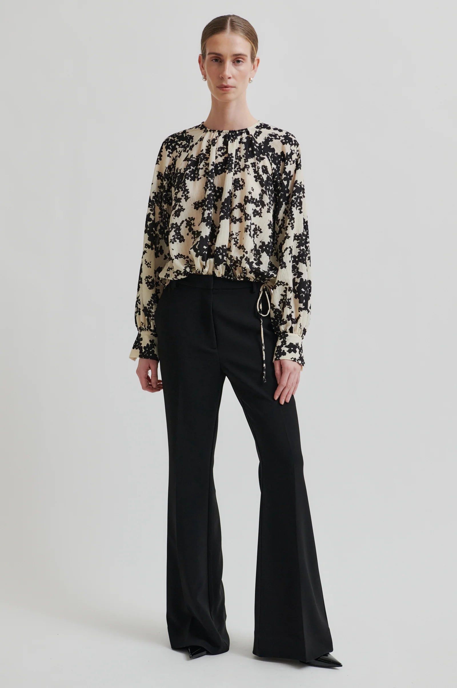 Women wearing a long sleeve cream blouse with black floral print and black pants on a white background