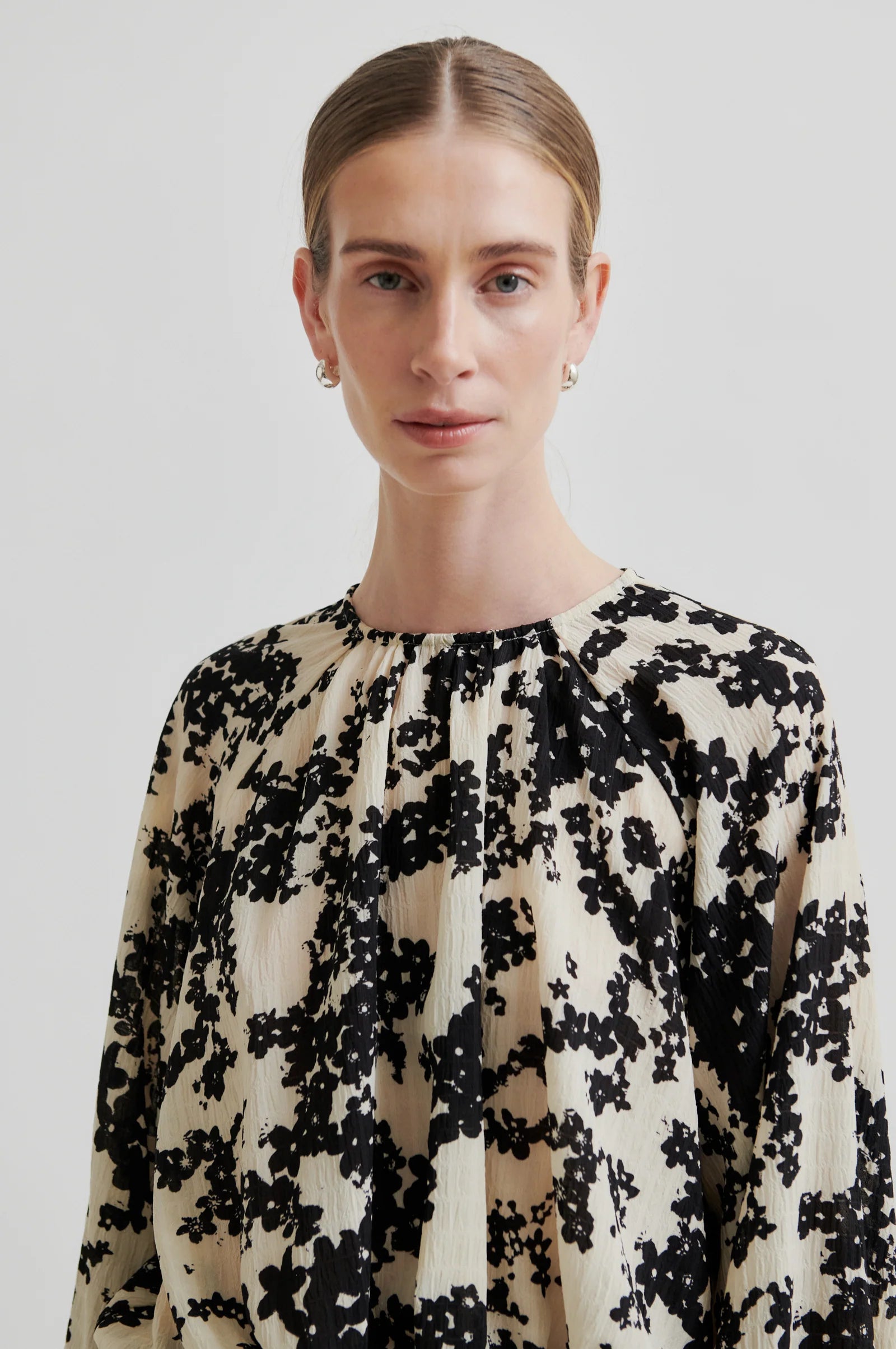 Women wearing a long sleeve cream blouse with black floral print on a white background