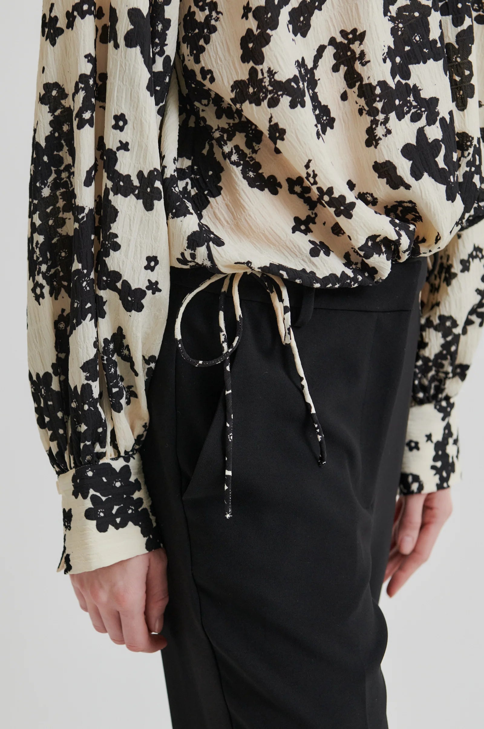Women wearing a long sleeve cream blouse with black floral print and black pants on a white background