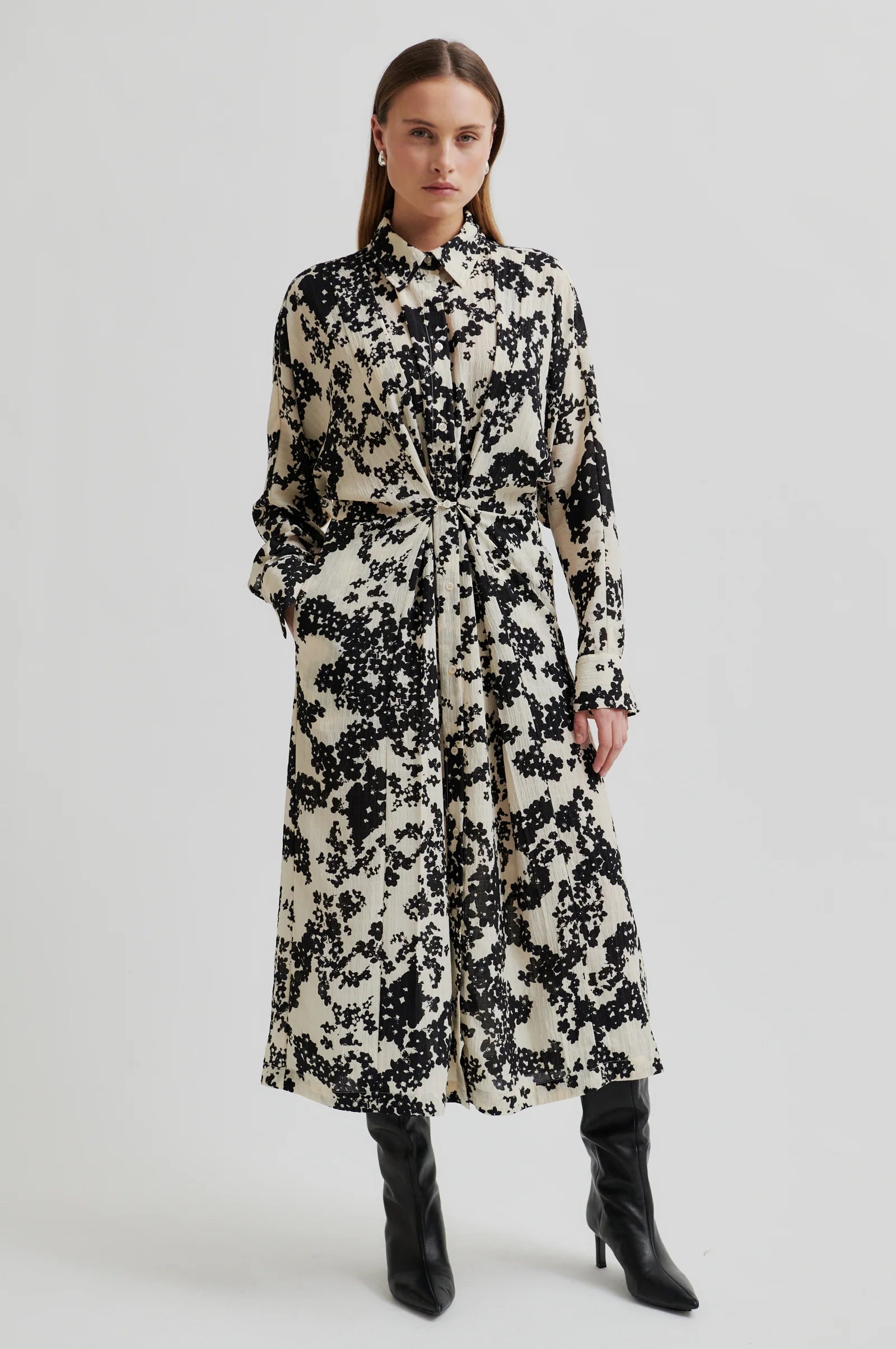 Woman wearing a midi length long sleeve dress with a cream base and black floral print on a white background. 