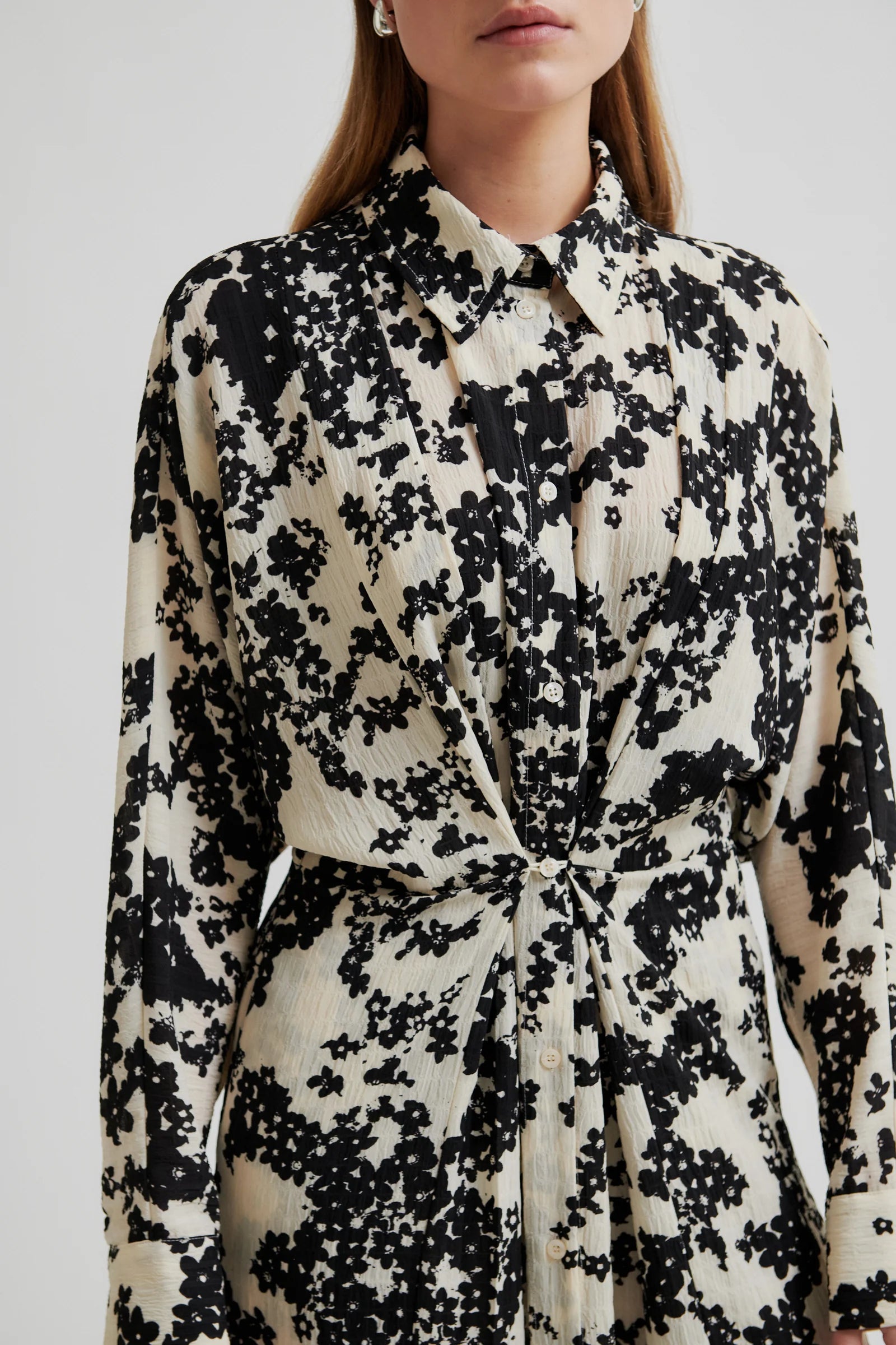Woman wearing a midi length long sleeve dress with a cream base and black floral print on a white background. 