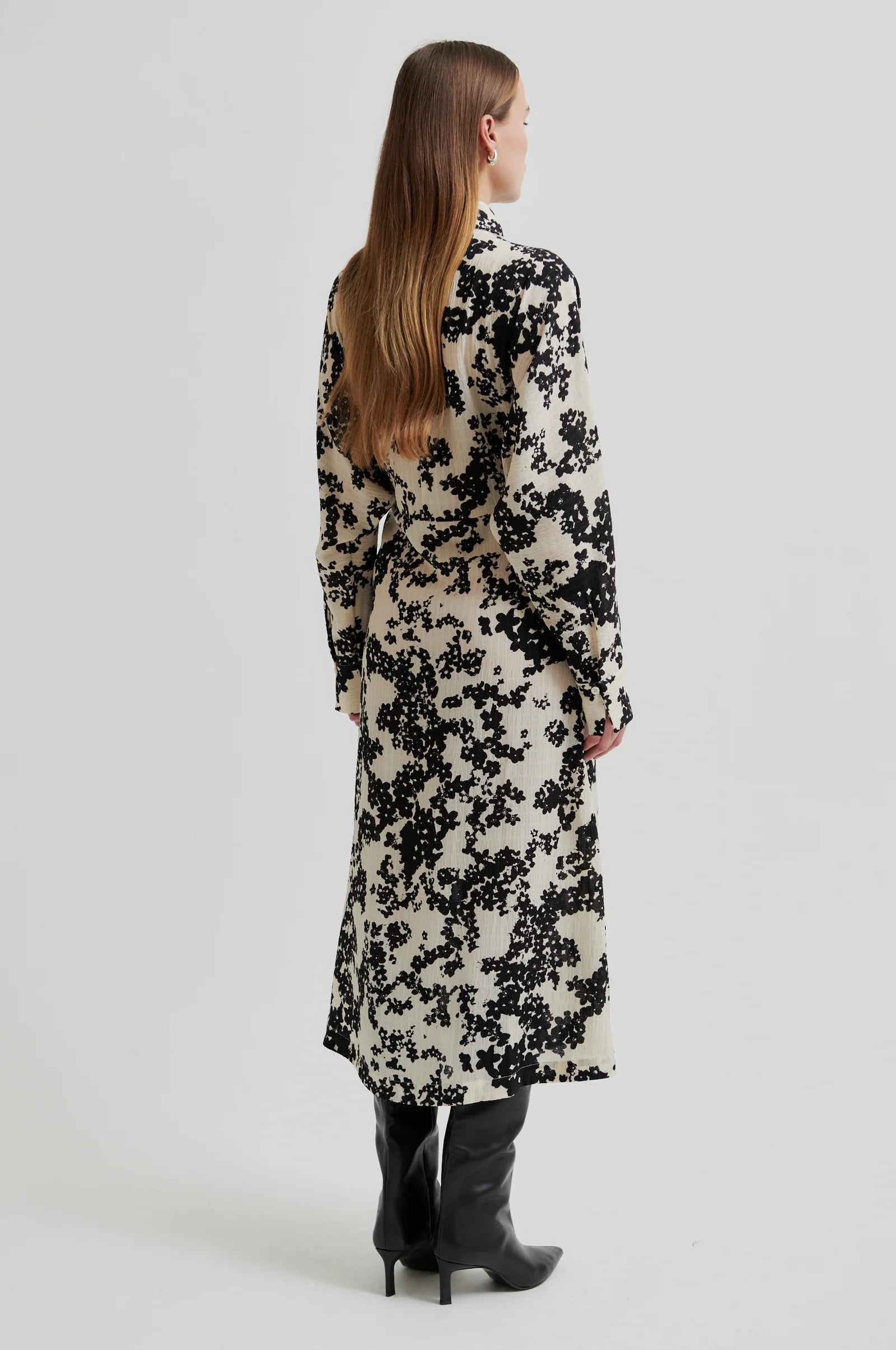 Woman wearing a midi length long sleeve dress with a cream base and black floral print on a white background. 