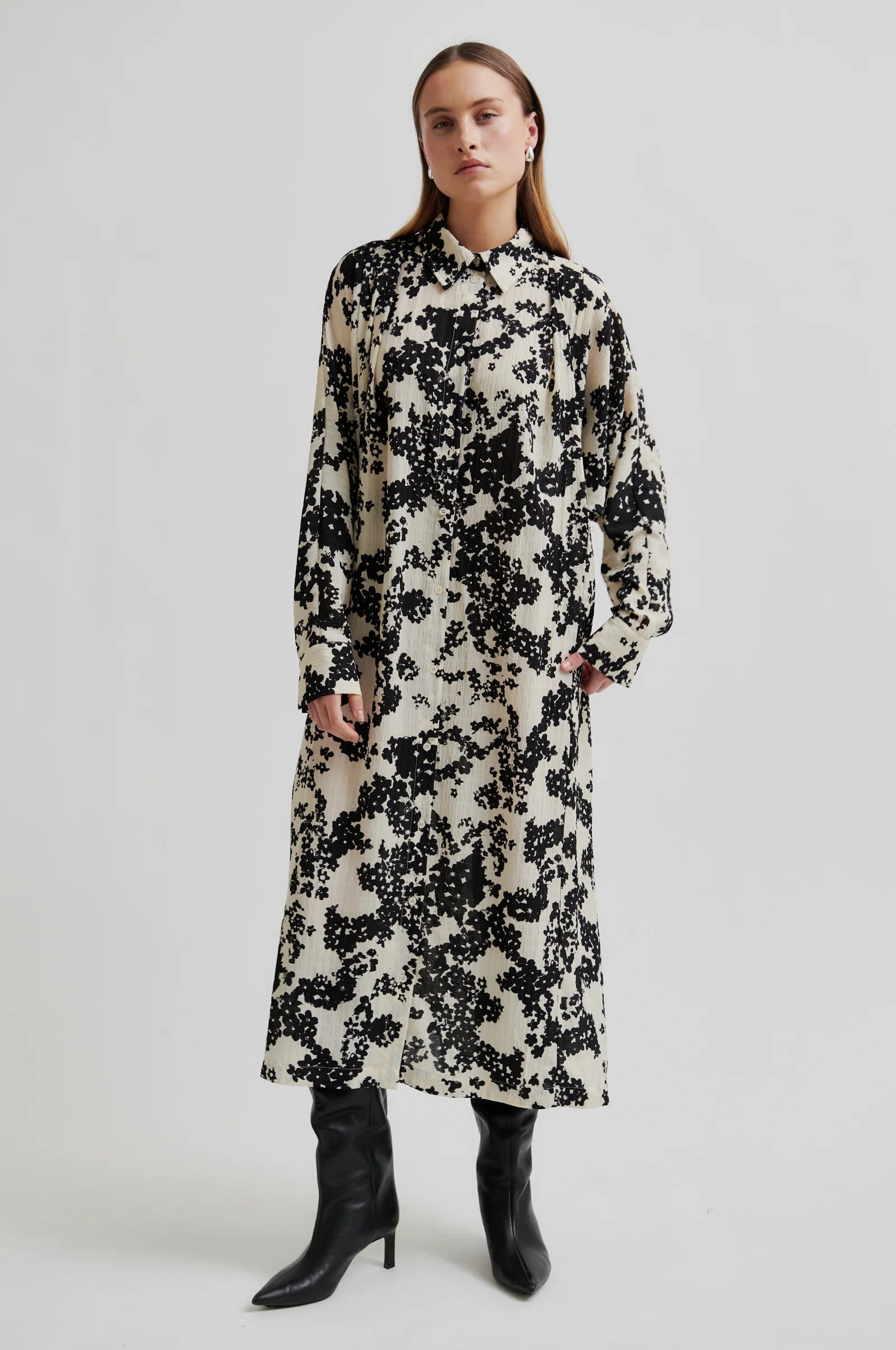 Woman wearing a midi length long sleeve dress with a cream base and black floral print on a white background. 