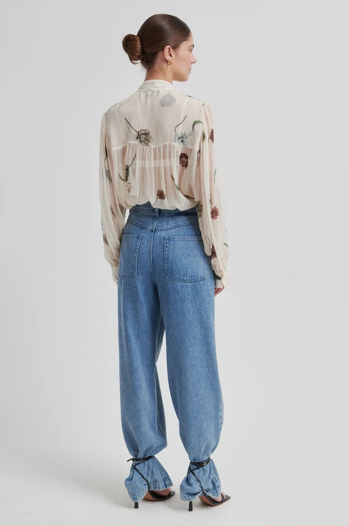 Model shown from back wearing a floral-patterned blouse  and denim pats with black heels on a neutral background