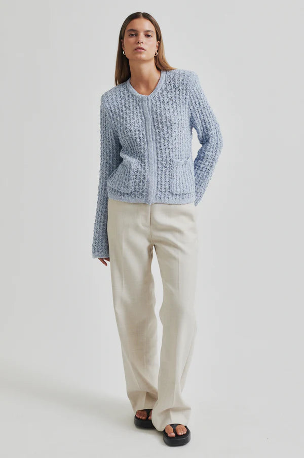 Model wearing a blue knitted cardigan and beige pants. 