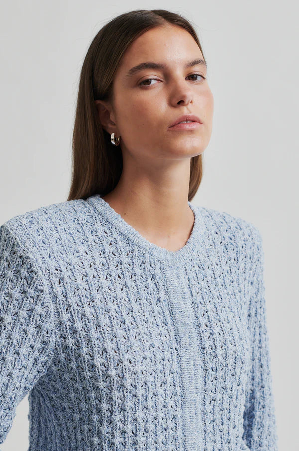 Model wearing a blue knitted cardigan and beige pants. 