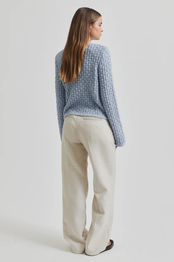 Model wearing a blue knitted cardigan and beige pants. 