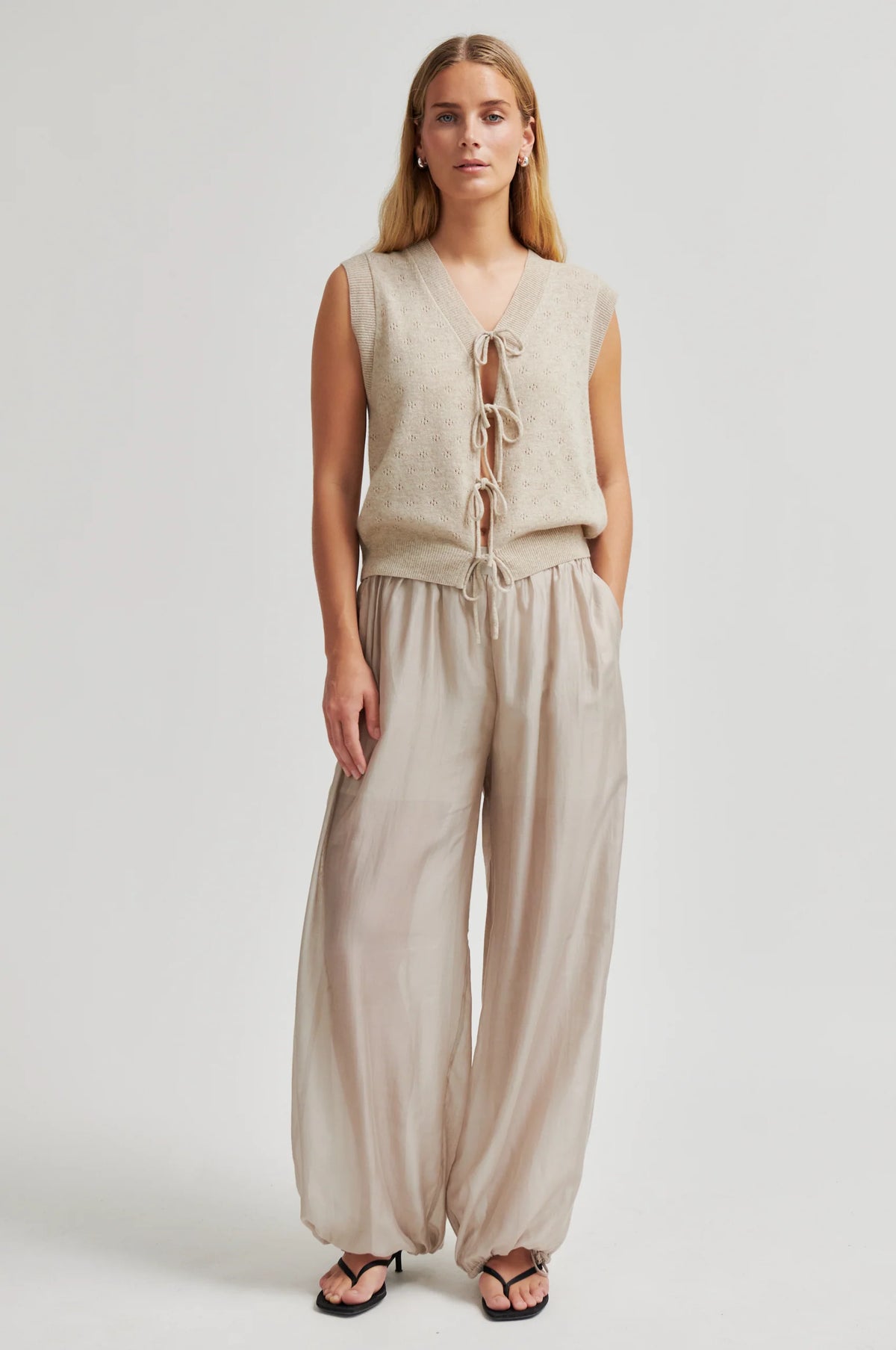 Woman wearing a beige sleeveless top and wide-leg pants on a white background