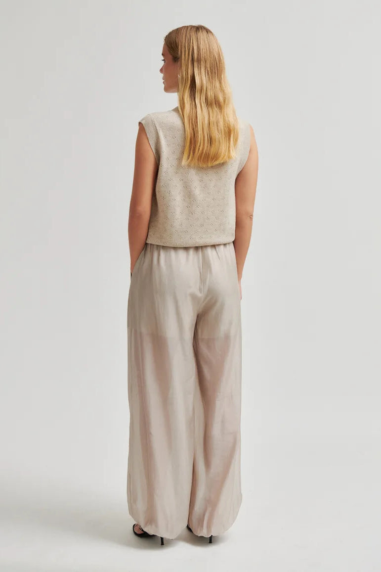 A woman shown from the back wearing a sleeveless textured light beige top and matching wide-leg trousers, photographed against a plain light gray studio background.
