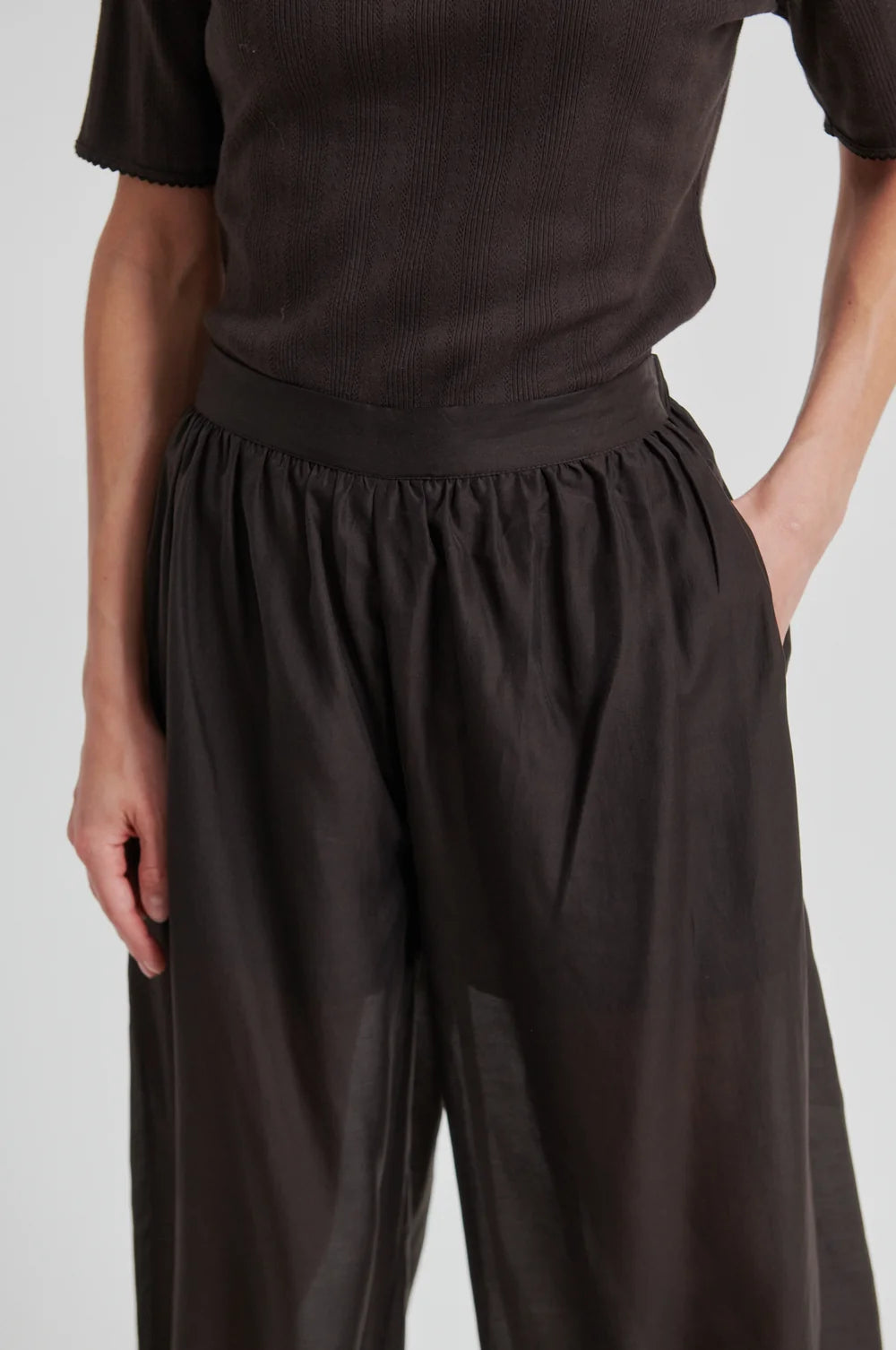 Model  up close wearing chocolate brown wide-leg pants  that taper and a matching top on a white background