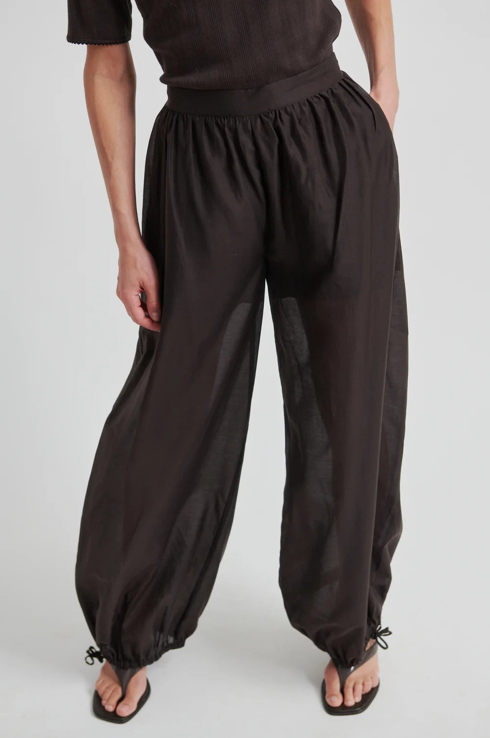 Model wearing chocolate brown wide-leg pants  that taper and a matching top on a white background