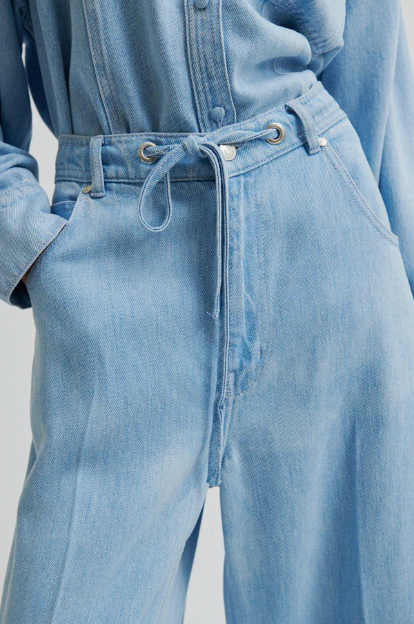 Model wearing light blue denim jean in drapy fabric with waist tie. 