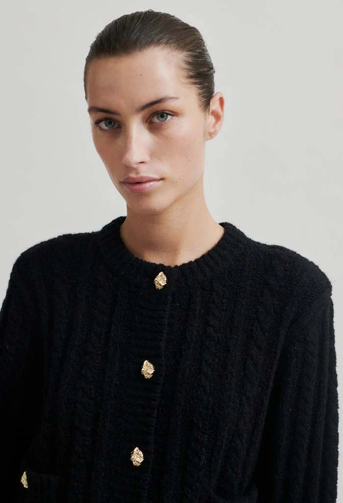 Black mock neck cardigan with gold button detail down front and on two front pockets at hip height.  Close up. 