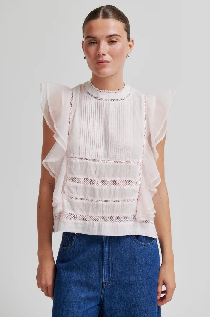 Woman wearing a white sleeveless top with sheer sleeves and blue jeans shorts on a light grey background