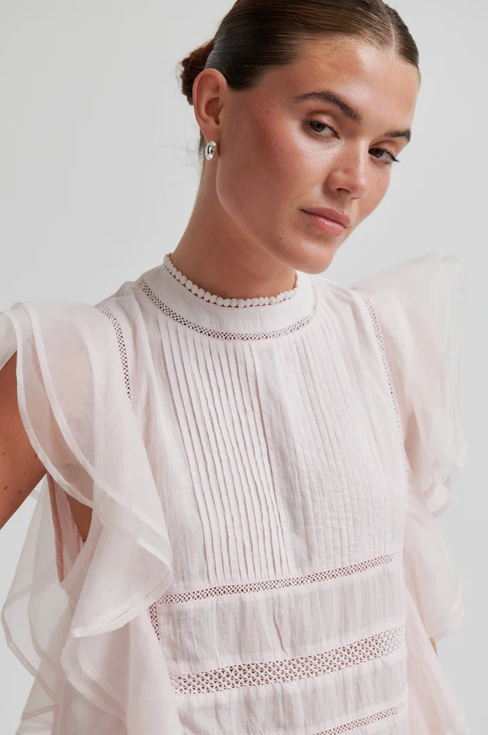 Woman close up wearing a white blouse with lace details on a light background
