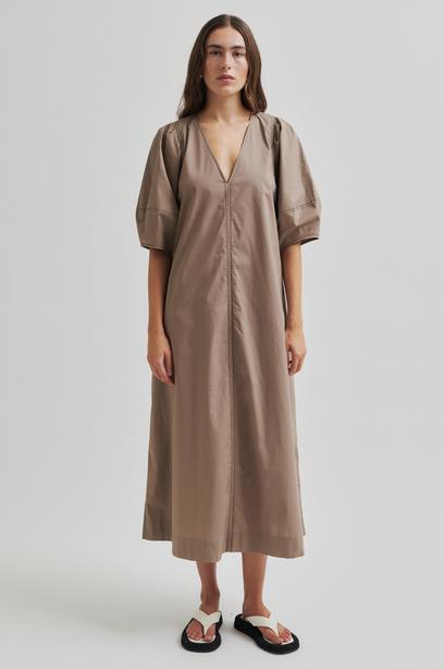 Woman wearing a beige Maxi dress with contrast stitching and short sleeves against a plain background