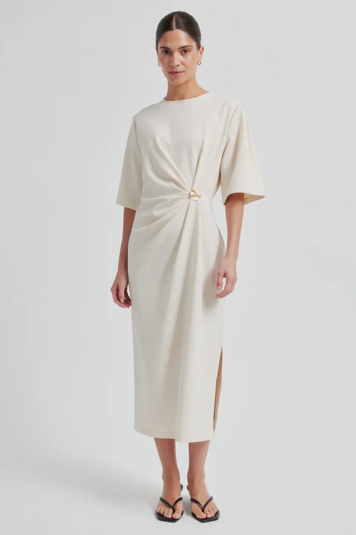 Woman wearing a white dress with a gold knot detail on a white background