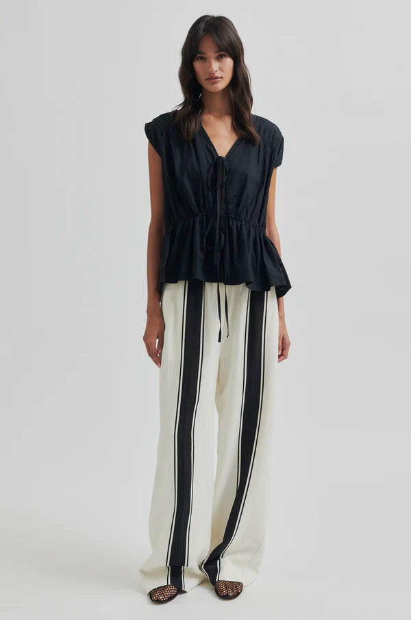 Woman wearing a black top and white pants with black stripes on a white background