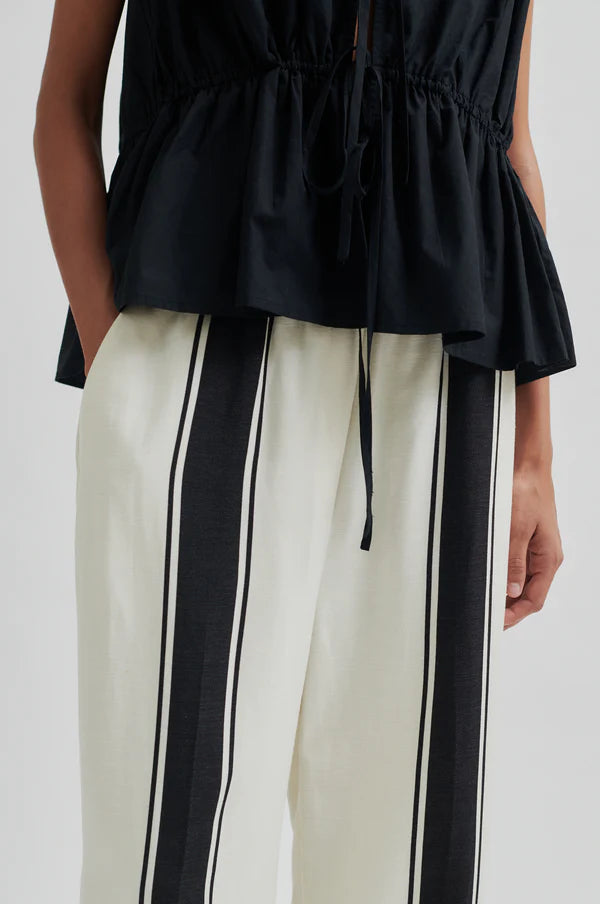 Black sleeveless top and white pants with black stripes on a white background