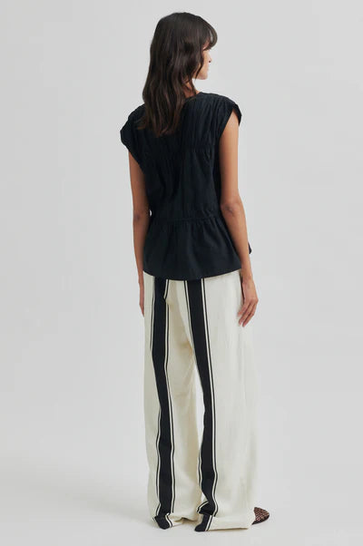 Woman wearing a black top and white pants with black stripes on a light gray background
