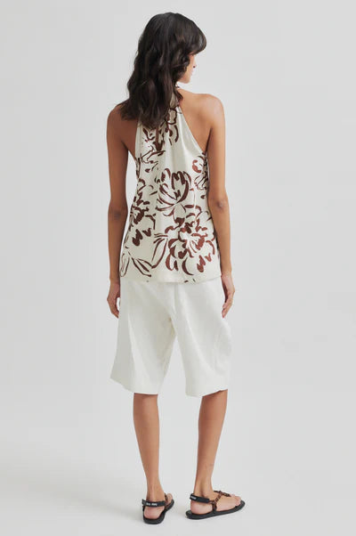 Woman wearing a floral halter top and white pleated shorts on a plain background