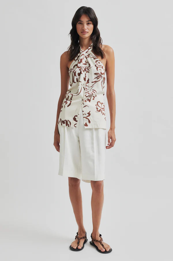 Woman wearing a floral halter top and white pleated shorts on a plain background