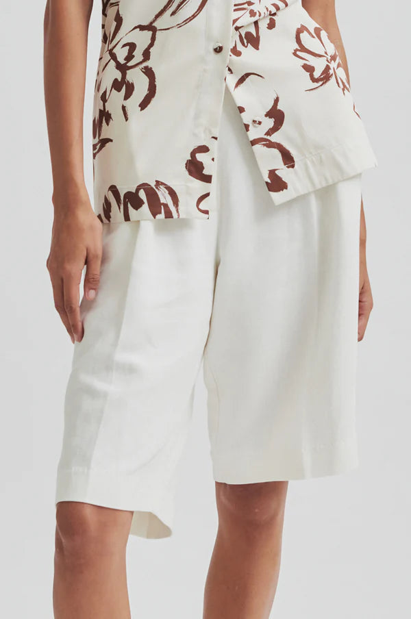 Woman wearing a floral halter top and white pleated shorts on a plain background