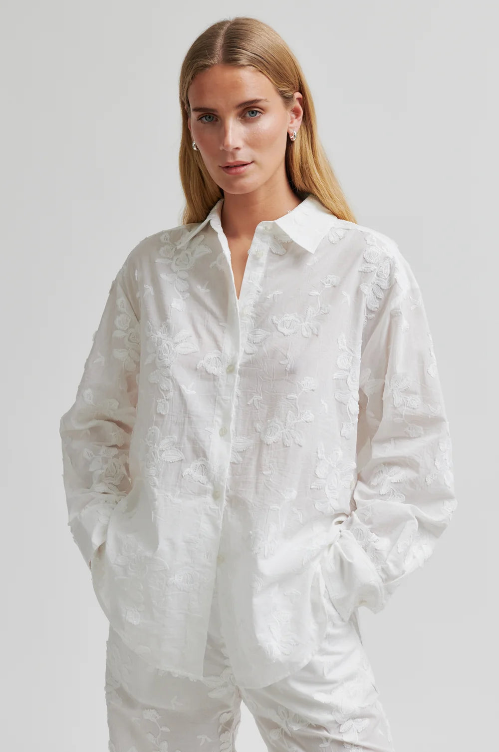 Woman wearing a white button-up shirt and pants on a plain background