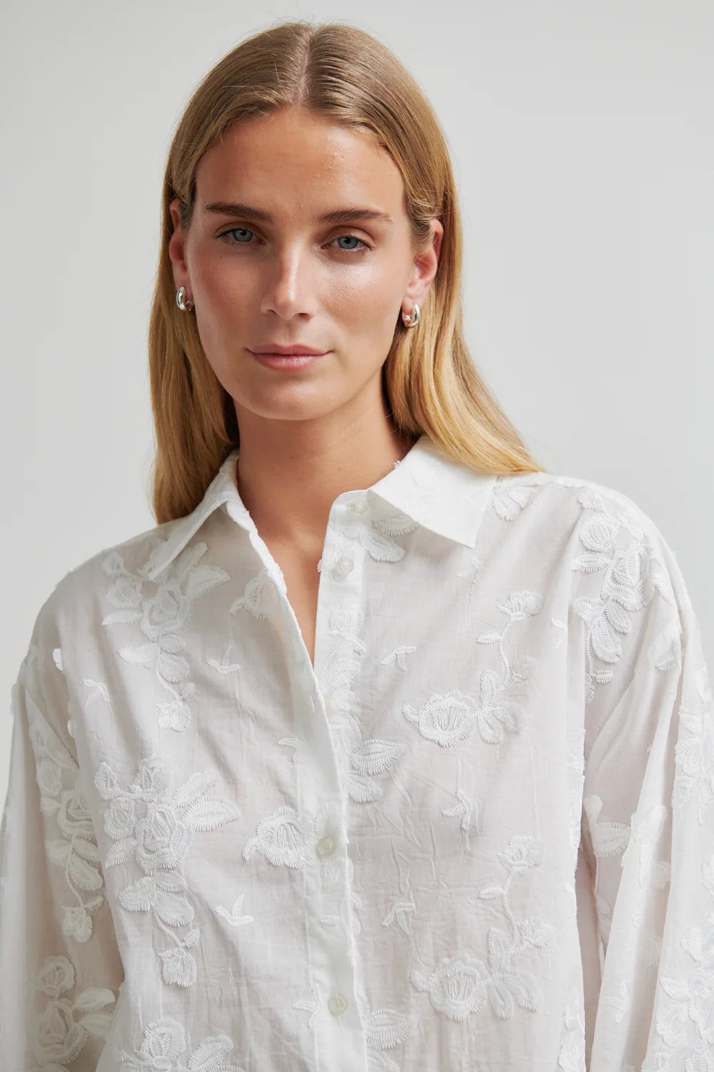 Woman wearing a white embroidered shirt against a plain background