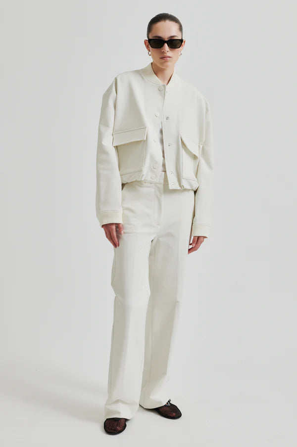 Model wearing drapy cream bomber jacket with front pockets. Paired with cream pants and black sunglasses. 