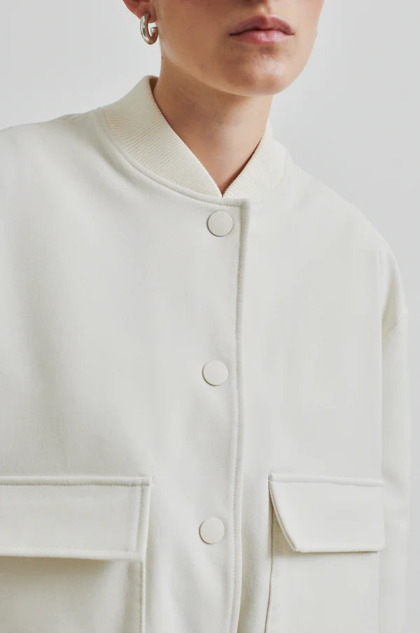 Model wearing drapy cream bomber jacket with front pockets. Paired with cream pants and black sunglasses. 