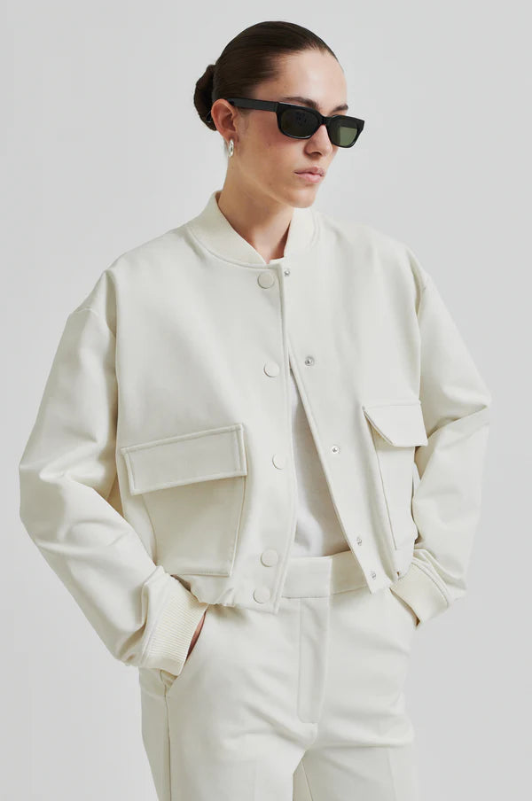 Model wearing drapy cream bomber jacket with front pockets. Paired with cream pants and black sunglasses. 