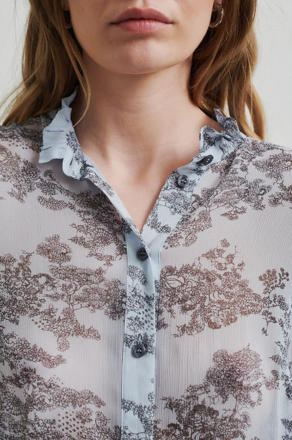 Model wearing soft blue sheer shirt with grey floral print paired with soft tan pants. 