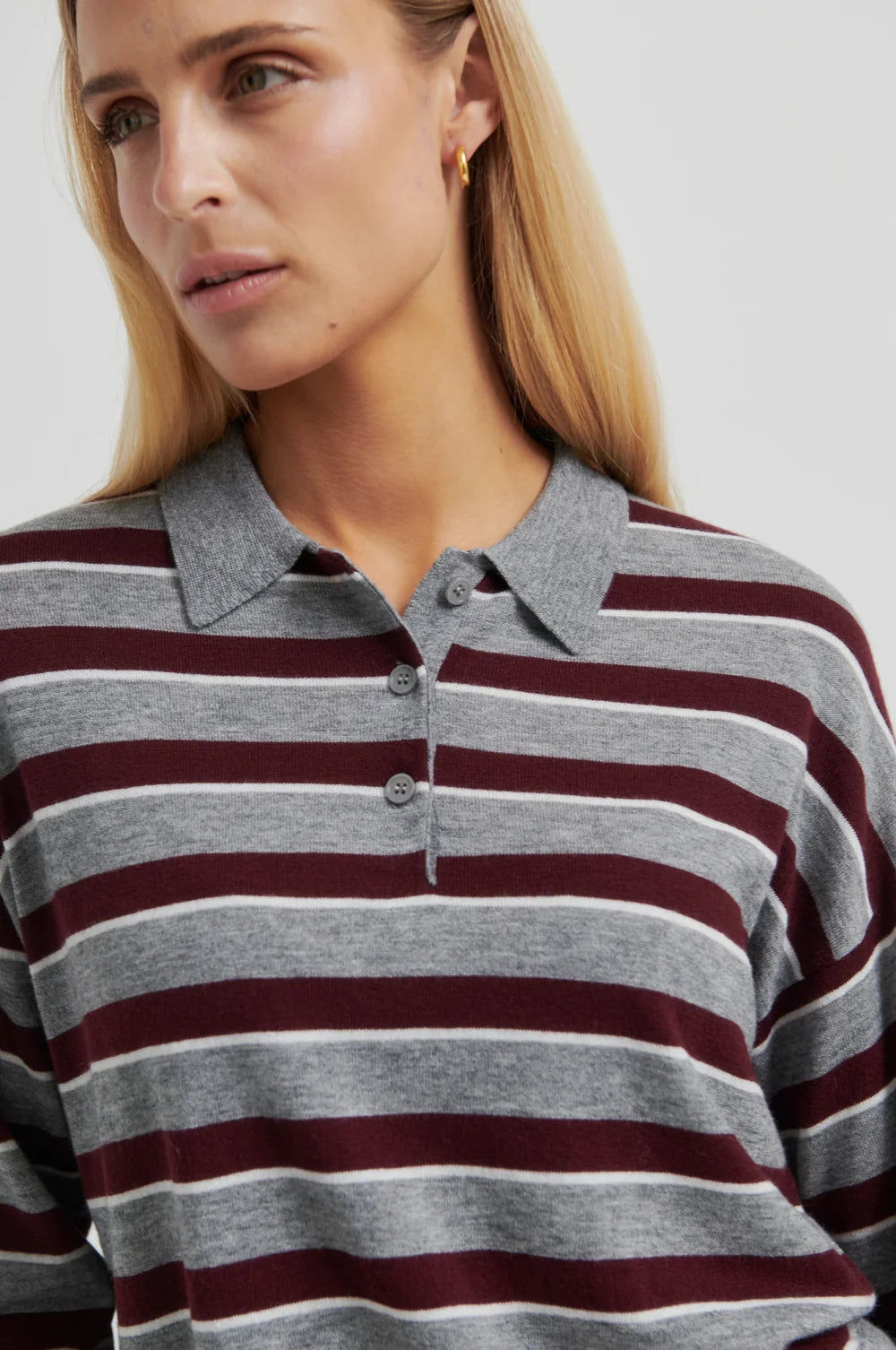 Women wearing a striped cropped polo sweater  in grey and brugandy with  on a plain background.  