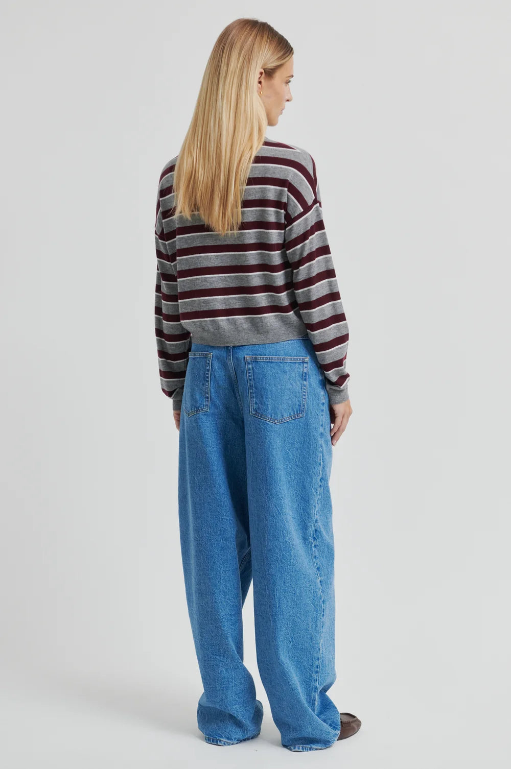 Women wearing a striped cropped polo sweater and jeans shown from the back on a plain background.  