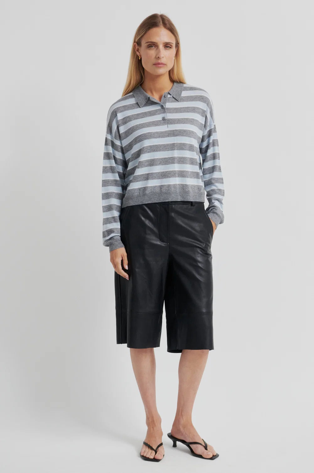 Woman wearing a grey and blue striped sweater with black pants on a light grey background