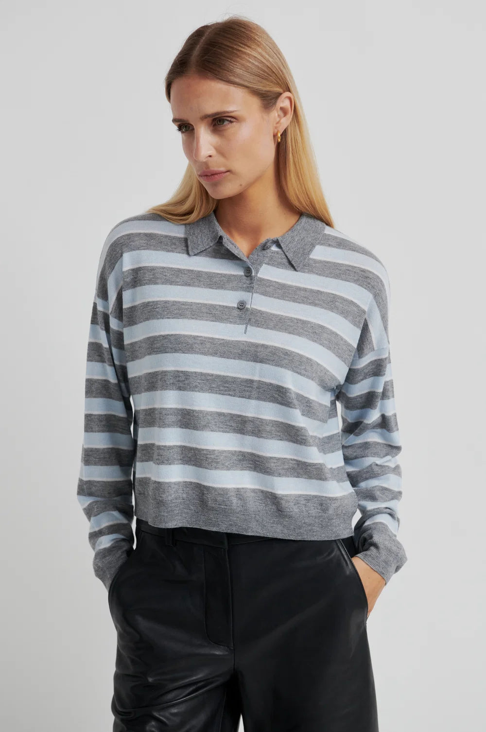 Woman wearing a grey and blue striped sweater with black pants on a light grey background