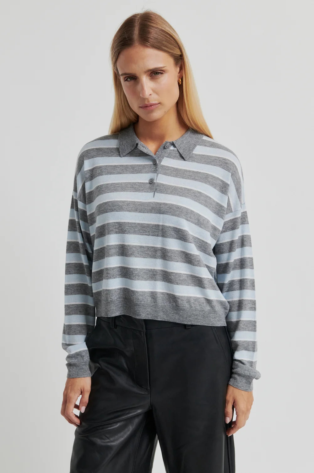 Woman wearing a grey and blue striped sweater with black pants on a light grey background