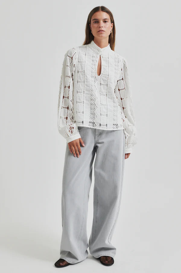 Model wearing broderie long sleeve off white blouse paired with soft grey denim jeans. 