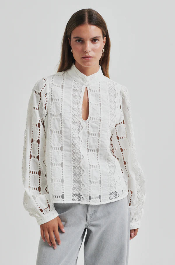 Model wearing broderie long sleeve off white blouse paired with soft grey denim jeans. 