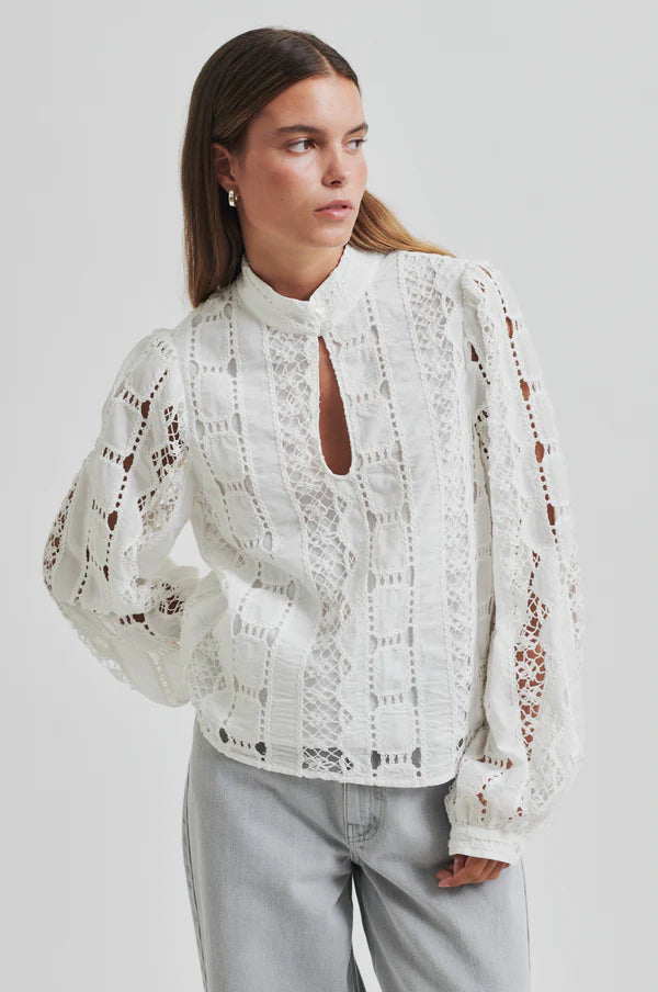 Model wearing broderie long sleeve off white blouse paired with soft grey denim jeans. 