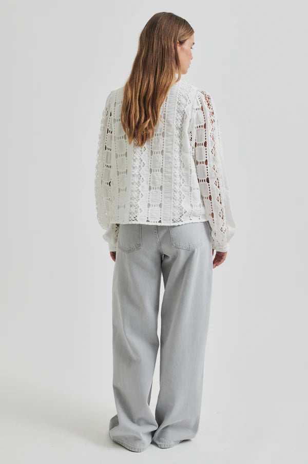 Model wearing broderie long sleeve off white blouse paired with soft grey denim jeans. 