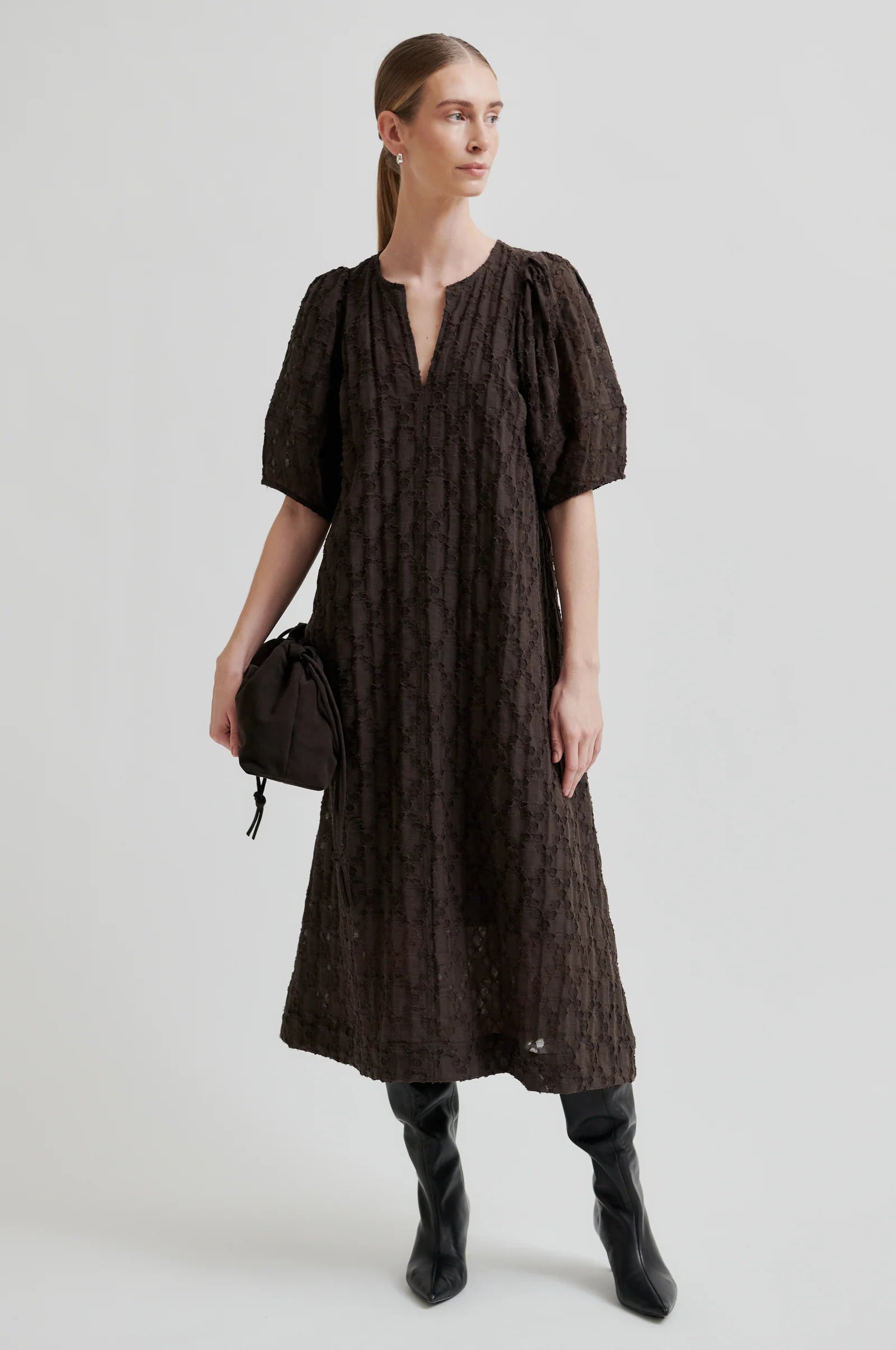Woman wearing a dark brown dress with short puff sleeves on a white background