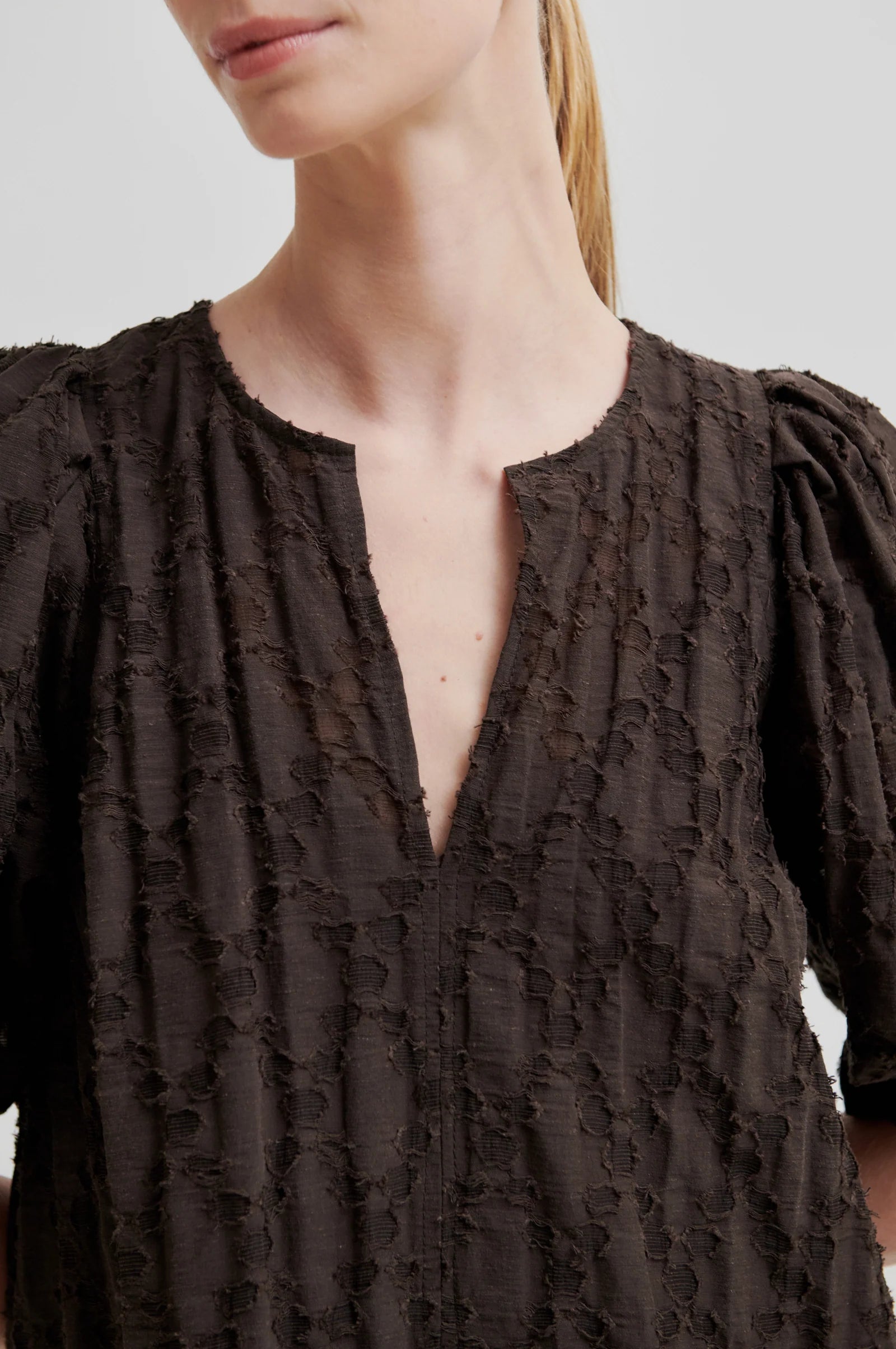 Woman wearing a dark brown dress with short puff sleeves on a white background