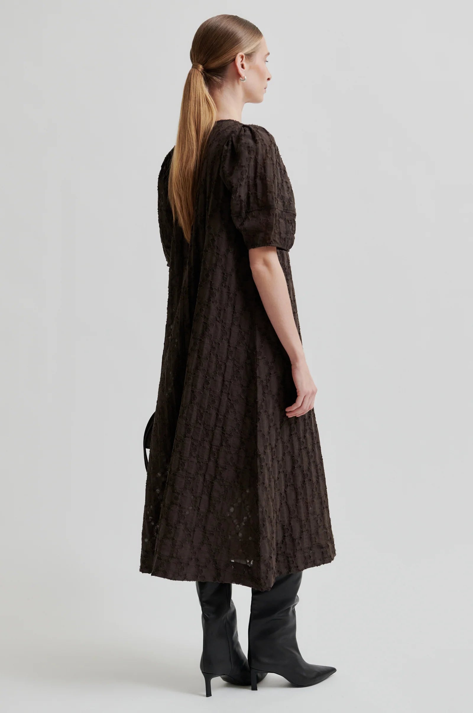 Woman wearing a dark brown dress with short puff sleeves on a white background